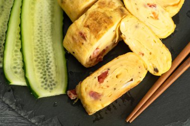 Geleneksel Japon omleti Tamagoyaki ve siyah tahta üzerinde salatalık dilimlenmiş yemek çubukları, yakın çekim