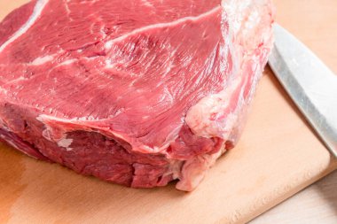 Tahta kesme tahtasının üzerinde büyük bir parça çiğ et ve aşçı bıçağı.