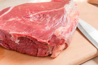 Tahta kesme tahtasının üzerinde büyük bir parça çiğ et ve aşçı bıçağı.