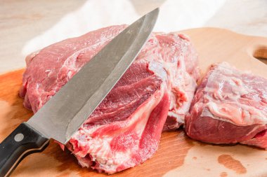 Ahşap kesme tahtasının üzerinde aşçı bıçağıyla bir parça et kesmek.