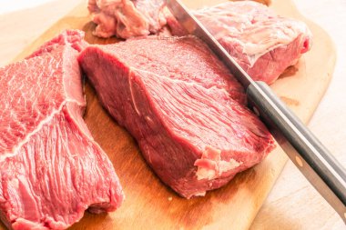 Ahşap kesme tahtasının üzerinde aşçı bıçağıyla bir parça et kesmek.