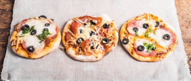 Birkaç hazır mini pizza, ahşap bir masada keten peçete üzerinde pizza.