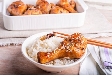 Bir kase pilav ve kızarmış tavuk, yapışkan tatlı soslu tavuk budu, susam tohumları, yemek çubukları ve kızarmış tavuk budu serpiştirilmiş parlak bir masa, Asya mutfağı..