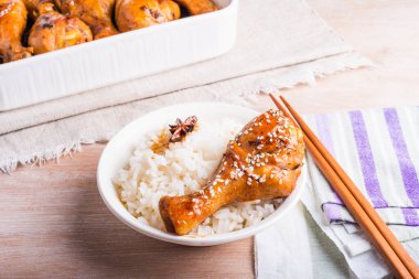 Bir kase pilav ve kızarmış tavuk, yapışkan tatlı soslu tavuk budu, susam tohumları, yemek çubukları ve kızarmış tavuk budu serpiştirilmiş parlak bir masa, Asya mutfağı..