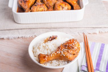 Bir kase pilav ve kızarmış tavuk, yapışkan tatlı soslu tavuk budu, susam tohumları, yemek çubukları ve kızarmış tavuk budu serpiştirilmiş parlak bir masa, Asya mutfağı..