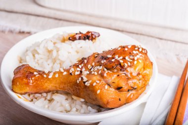 Bir kase pilav ve tavuk budu yapışkan tatlı bir sosta kızartılmış, susamlı, yakın plan Asya mutfağı serpiştirilmiş.