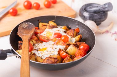 Erkekler kırsal kahvaltısı - tavada yumurta ve kiraz domatesli kızarmış patates, ahşap mutfak masasında duruyor..