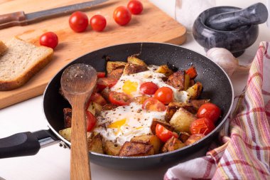 Erkekler kırsal kahvaltısı - tavada yumurta ve kiraz domatesli kızarmış patates, ahşap mutfak masasında duruyor..