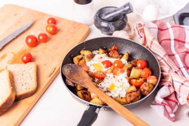 Erkekler kırsal kahvaltısı - tavada yumurta ve kiraz domatesli kızarmış patates, ahşap mutfak masasında duruyor..