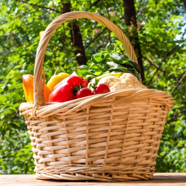Güneşli bir günde bahçedeki ağaçların arka planında, ahşap bir masada olgun sebzelerle dolu sepet. Yakın plan.