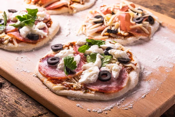 Cooking traditional Italian mini pizza, pizzetta - raw mini pizza with sausage and mozzarella cheese on a chopping board