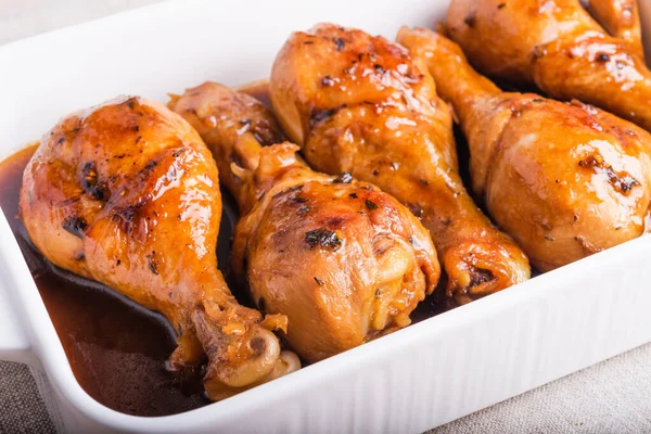 stock image Chicken drumstick baked in sweet soy sauce in white ceramic baking dish, close-up.