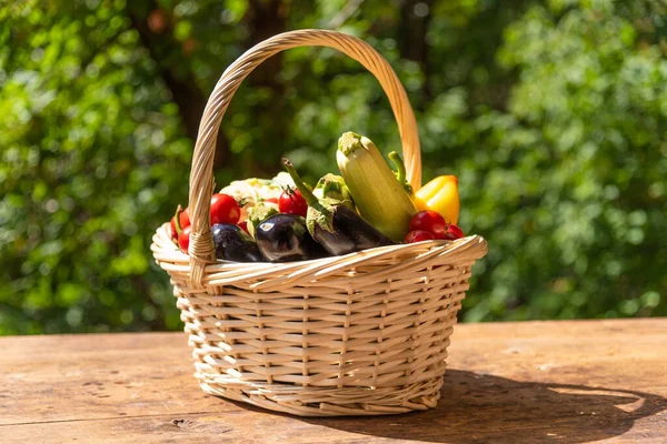 Olgun sebzelerle dolu sepet, bahçedeki ağaçların arka planında, ahşap bir masanın üzerinde.