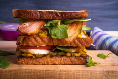 Lezzetli bir köy sandviçi. Tavuklu kızarmış ekmek, kızarmış pastırma, domates, soğan, hardallı turşu ve ahşap tahta üzerinde roka salatası.
