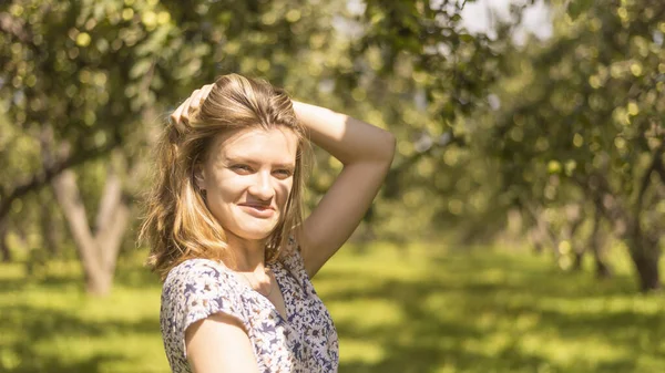 庭の背景に明るい太陽に照らされた若い魅力的な幸せな女性 — ストック写真