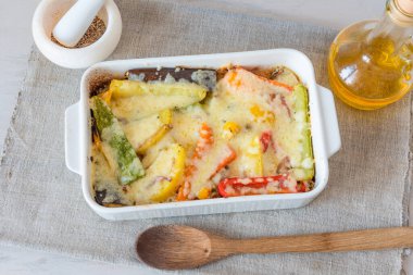 Beyaz seramik fırında peynirle pişirilmiş sebzeler. Vegan mutfağı.