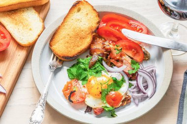 Taze köy kahvaltısı. Domuz pastırmalı, soğanlı ve domatesli sahanda yumurta. Hafif ahşap arka planda tost.
