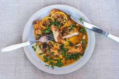 Kızarmış tavuk göğsü, limon dilimleri ve lezzetli bir sos, masanın üstünde peçete, çatal ve bıçakla birlikte.