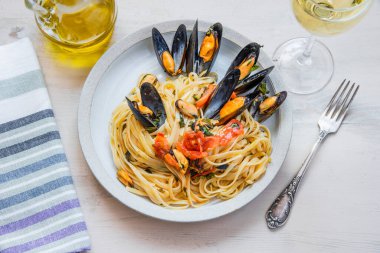İtalyan yemeği, tabakta midye ve arka planda beyaz şarap olan linguine makarna.