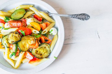 Yemek masasının üstündeki tabakta Margarita makarna tarifi için kopyalama alanı domatesli makarna, kabak, mozzarella ve fesleğen..