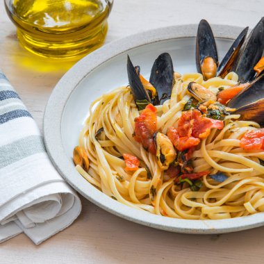 İtalyan yemeği, tabakta midye ve arka planda beyaz şarap olan linguine makarna.
