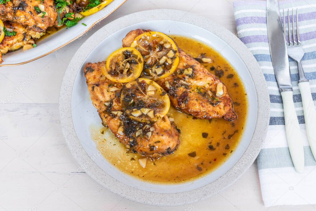 Chicken francese - Fried chicken breast with lemon slices and delicious sauce on a white plate on the table with a napkin, fork and knife, top view