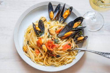 İtalyan yemeği, tabakta midye ve arka planda beyaz şarap olan linguine makarna.
