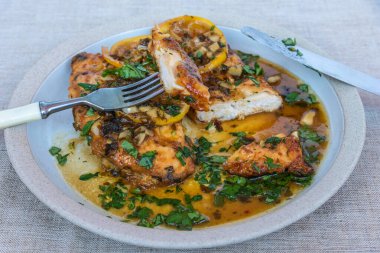 Kızarmış tavuk göğsü, limon dilimleri ve beyaz tabakta lezzetli bir sos.