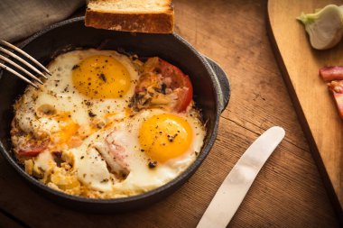 Kırsal kesimlerde çırpılmış yumurta, domates ve soğan kırsal ahşap bir masada dökme demir bir tavada.