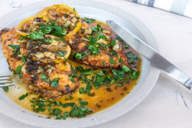 Kızarmış tavuk göğsü, limon dilimleri ve beyaz tabakta lezzetli bir sos.