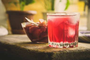 Kırsal bir masada buzlu kırmızı meyve suyu ve şuruplu bir bardak elma.