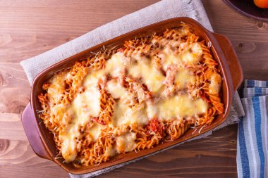 Ahşap arka planda pişirmek için mozzarella ve domatesli fırınlanmış fusilli makarna..