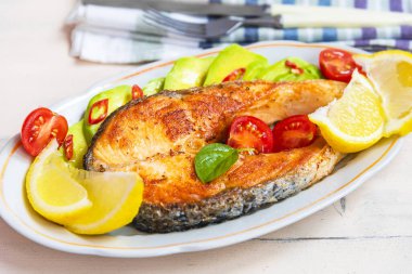 Avokado ve limonlu bir tabakta kızarmış somon bifteği.