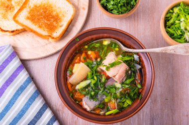 Patates, domates ve havuçlu somon fileto balığı çorbası yeşil soğan ve maydanoz serpiştirilmiş ahşap bir masada parlak bir tabak, üst manzara