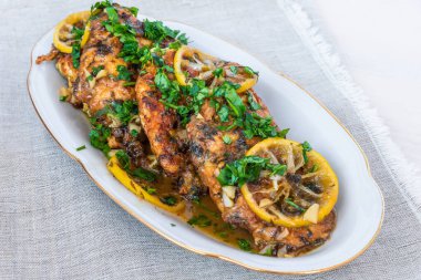 Kızarmış tavuk göğsü, limon dilimleri ve beyaz tabakta lezzetli bir sos.