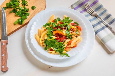 İtalyan yemeği - biberli, domatesli makarna ve arka planda bir tabakta maydanoz, makarna.