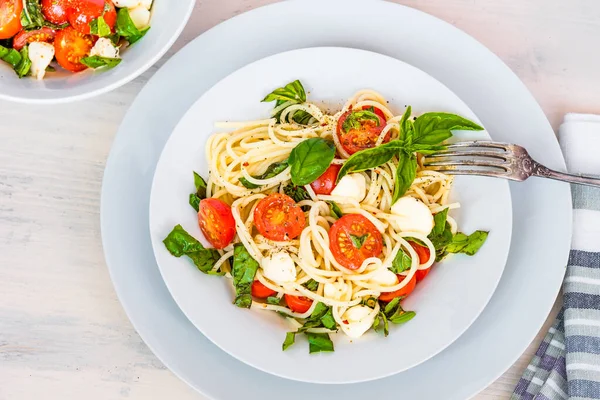 Italian food - Spaghetti caprese in a plate on a light rustic background, top view. Pasta with mozzarella, cherry tomatoes and basil