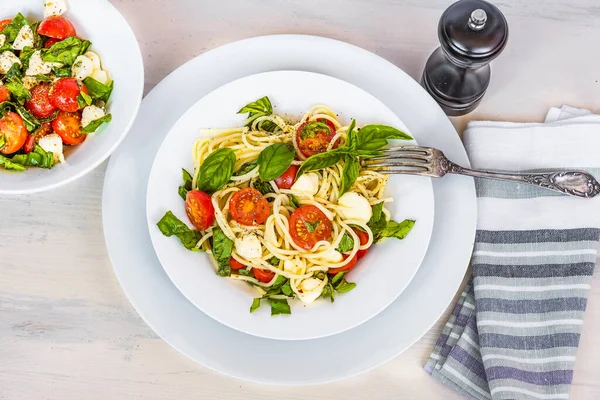 Italian food - Spaghetti caprese in a plate on a light rustic background, top view. Pasta with mozzarella, cherry tomatoes and basil