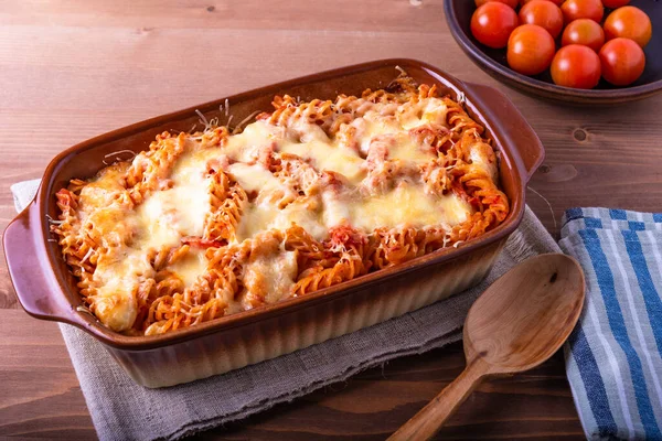 Ahşap arka planda pişirmek için mozzarella ve domatesli fırınlanmış fusilli makarna..
