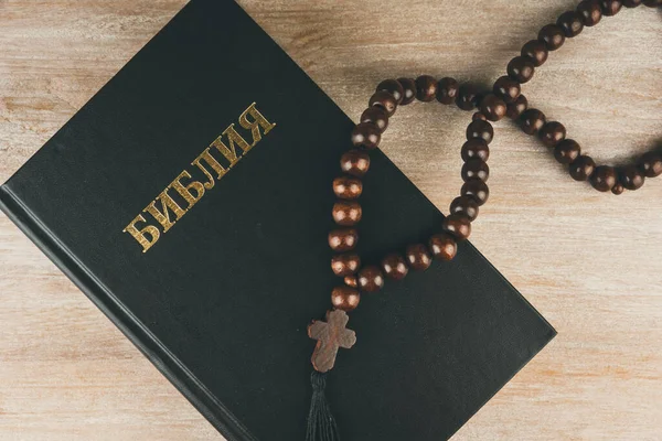 Russian Bible and rosary on a rustic wooden table