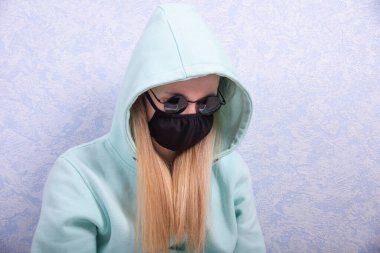 Siyah virüs koruyucu maskeli, siyah gözlüklü ve kapüşonlu ceketli genç bir kadın evdeki bilgisayarda çalışıyor. Evde uzaktan çalışma kavramı