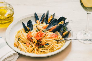 İtalyan yemeği, tabakta midye ve arka planda beyaz şarap olan linguine makarna.
