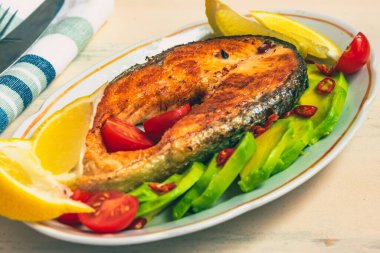 Avokado ve limonlu bir tabakta kızarmış somon bifteği.