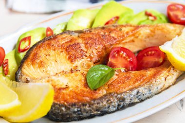 Avokado ve limonlu bir tabakta kızarmış somon bifteği.