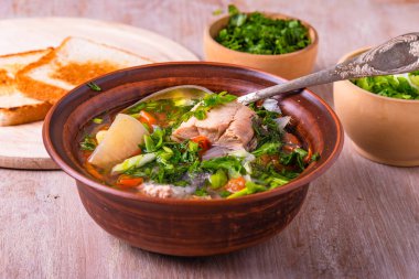 Patates, domates ve havuçlu somon fileto balığı çorbası yeşil soğan ve ahşap bir masada parlak bir tabakta maydanoz serpiştirilmiş.