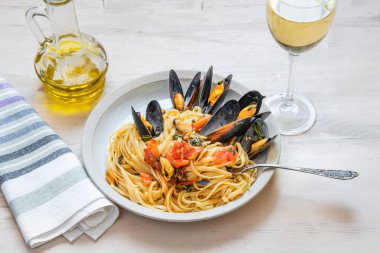 İtalyan yemeği, tabakta midye ve arka planda beyaz şarap olan linguine makarna.