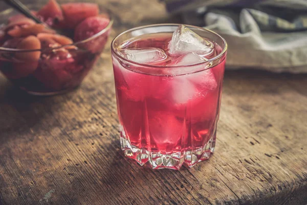 Red fruit drink with ice on an old rustic table with a cup of apples in syrup