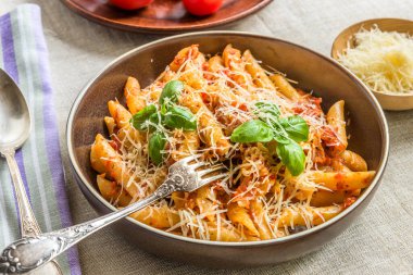 Makarna All 'Arrabbiata, domates soslu makarna, fesleğen ve parmesan peyniri ahşap masa üzerinde keten peçeteyle.