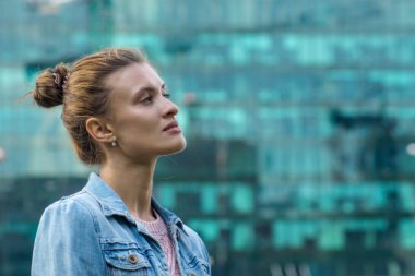 Bir ofis binasının arka planında profili olan genç bir kadın.