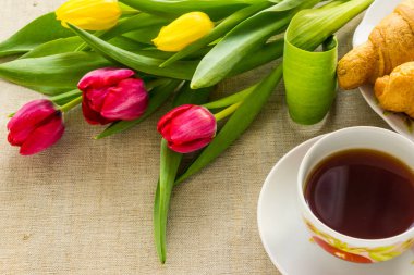 Masada bir fincan kahve ve kruvasan ve yakın plan laleler, fotokopi alanı - konsept selamlama